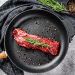 Raw strip vegas steak in a pan with cooking ingredients. Gray background. Top view