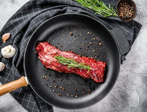 Raw strip vegas steak in a pan with cooking ingredients. Gray background. Top view
