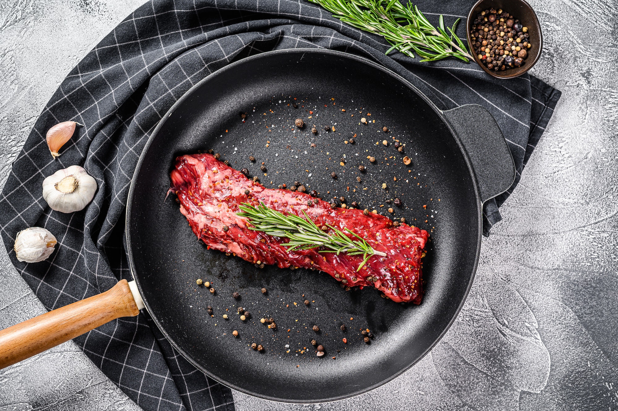 Raw strip vegas steak in a pan with cooking ingredients. Gray background. Top view